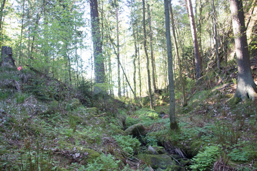 Bäcken rinner i en liten ravin, högt uppe till vänster i bild skymtar ett par golfspelare som är på väg mot nästa hål.
