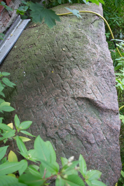 Vid gaveln av stallet ligger denna moderna runsten, runor med en grekisk dikt! Foto: Per Hallén 2015